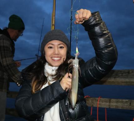 A young woman holds up a squid she caught.